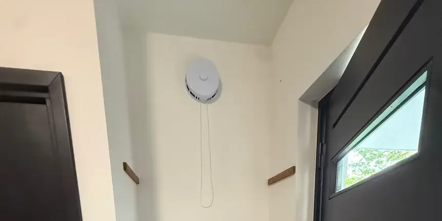 Zelfregelend toevoerventiel hoog op de muur van een gang, ruim boven 1,8 meter, met een koord om het te bedienen